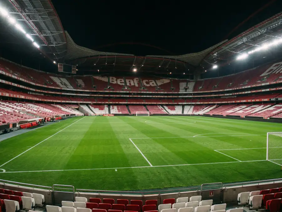 Estádio de futebol português visto de dentro com campo verde iluminado e adeptos nas bancadas
